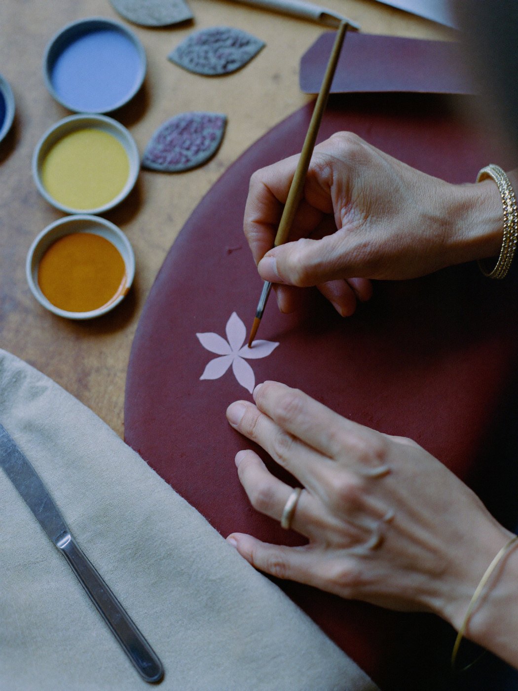 A Persian flower being painted onto burgundy leather at the studio bench